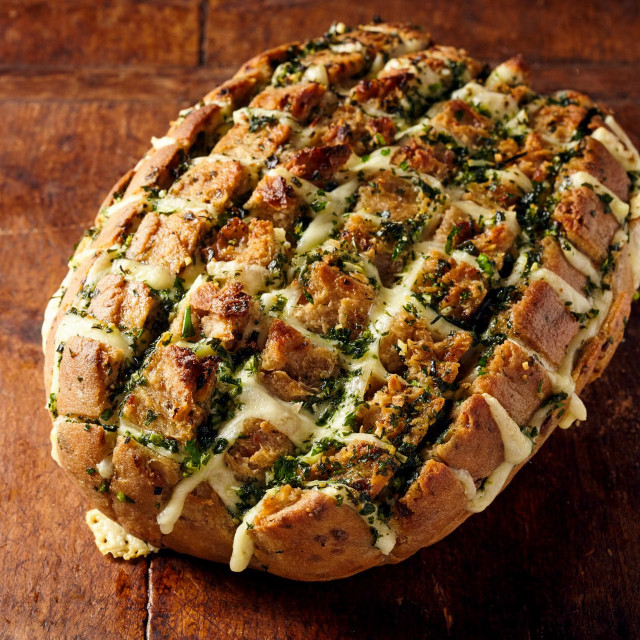 Single freshly baked loaf of party bread with cheese stuffing dripping from sliced surface over rustic wooden table with copy space
