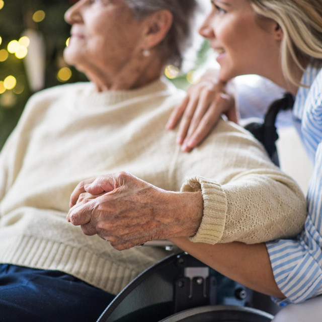 A senior woman in wheelchair with a health visitor at home at Christmas time.
