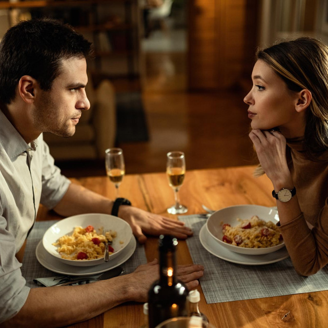 Young couple having problems in their relationship and talking during a meal at dining table.
