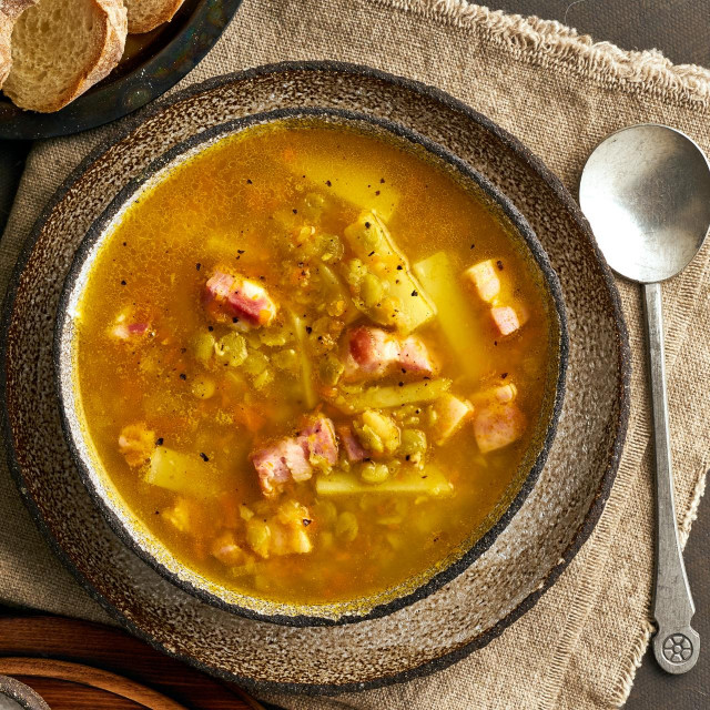 Winter hot soup with chopped green peas, pork, bacon, smoked on a dark brown wooden table. Delicious appetizing fat rich soup.