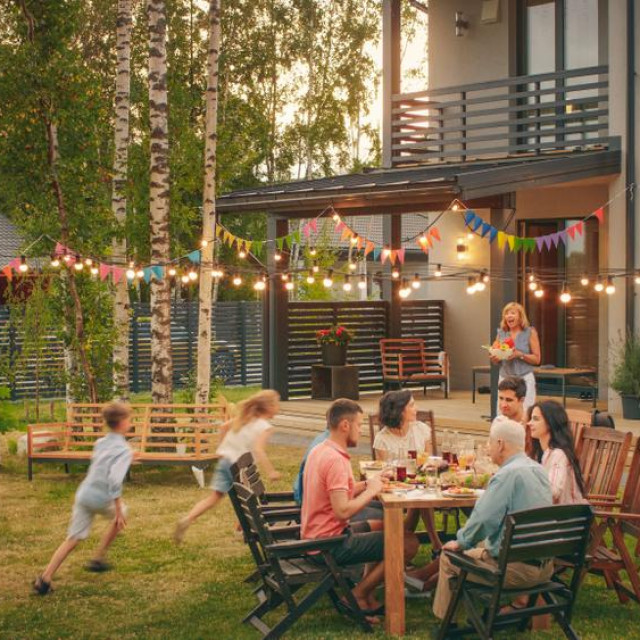 Big Family Garden Party Celebration, Gathered Together at the Table Family, Friends and Children. People are Drinking, Passing Dishes, Joking and Having Fun. Kids Run Around Table.
