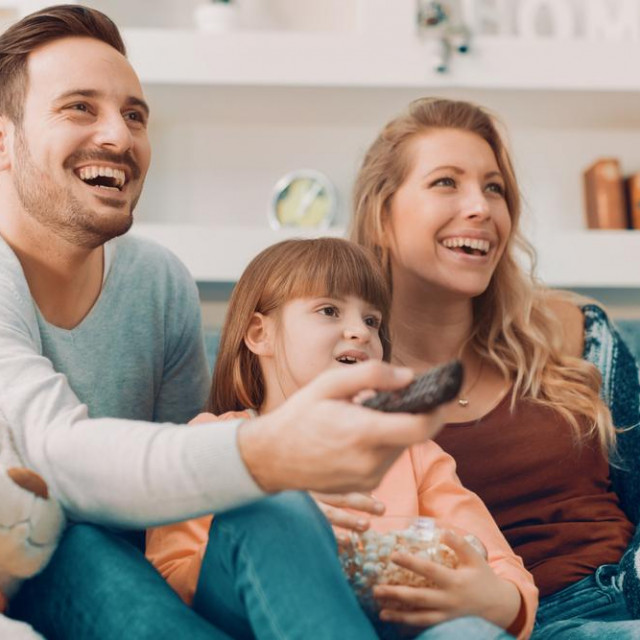 Young family watching TV together at home and having fun together.