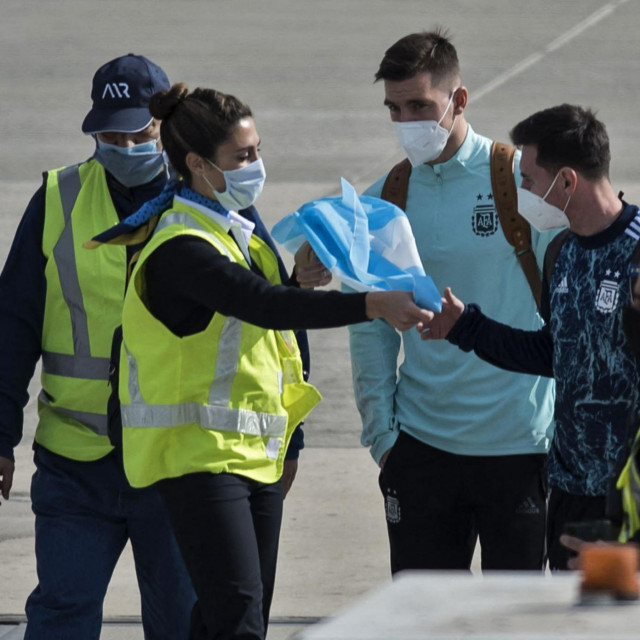 (FILES) In this file photo taken on July 11, 2021 a worker gives an Argentinian flag to Argentina's Lionel Messi (2-R), next to teammate Giovani Lo Celso (3-R), upon their arrival at the Islas Malvinas airport in Rosario, Santa Fe province, Argentina, after Argentina won the 2021 Copa America final football match against Brazil. - Forty years after the Falklands/Malvinas war Argentina continues to claim sovereignty over the islands, which the country's then military junta invaded on April 2, 1982. More than 900 people died, including 655 Argentines, 255 British troops and three islanders, before Argentine forces surrendered on June 14, 1982. Argentina returned to democracy in 1983. (Photo by AFP)