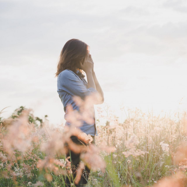 Sad woman standing in field with sunset background.
