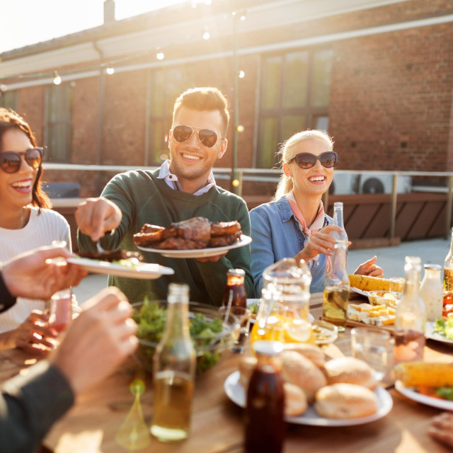leisure and people concept - happy friends eating and drinking at barbecue party on rooftop in summer