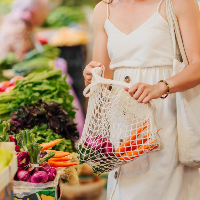 Young Woman puts fruits and vegetables in cotton produce bag at food market. Reusable eco bag for shopping. Zero waste concept.