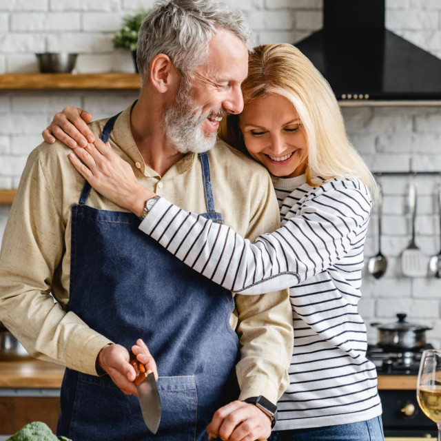 Beautiful mature couple hugging while cooking vegetable salad at kitchen table