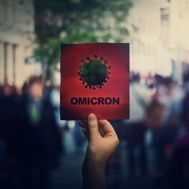 Omicron the new variant of the Covid-19 virus, coronavirus mutations, sars-cov-2 strain. Hand holds red banner warning in the crowded streets. Another wave of pandemic outbreak