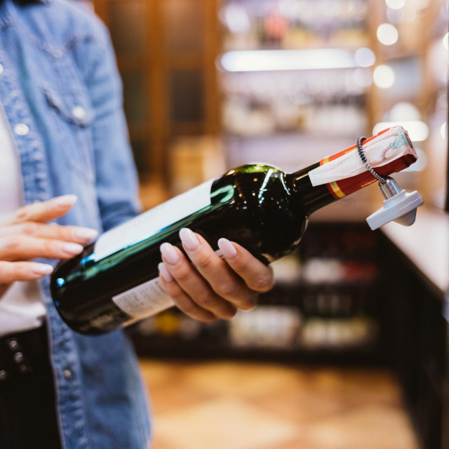 Close-up female hands holding bottle of wine in supermarket.