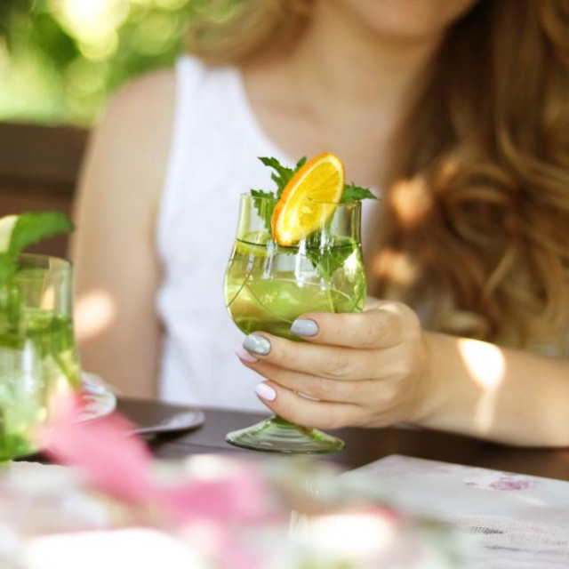 A girl with a glass sits in a cafe. A glass of lemonade in the hands of a girl.