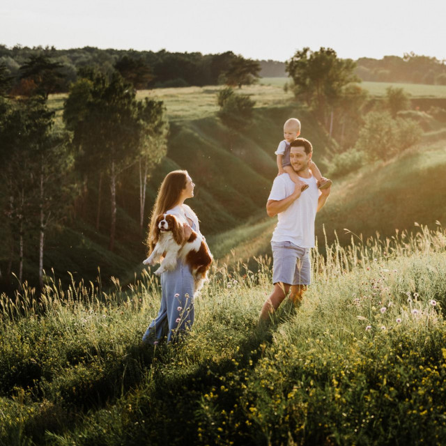 Young beautiful family with a little daughter hug, kiss and walk in nature. Photo of a family with a small child in nature.
