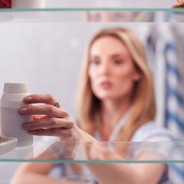 View Through Bathroom Cabinet Of Young Woman Taking Medication From Container