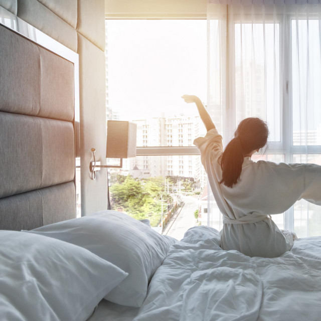 Hotel room comfort with good sleep easy relaxation lifestyle of Asian girl on bed have a nice day morning waking up, taking some rest, lazily relaxing in guest bedroom in city hotel