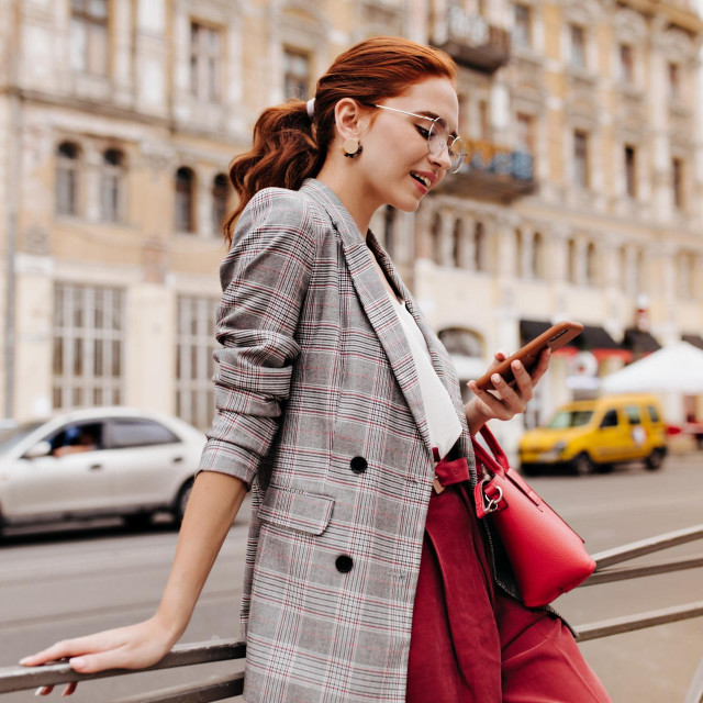 Red haired woman in stylish outfit chatting on phone