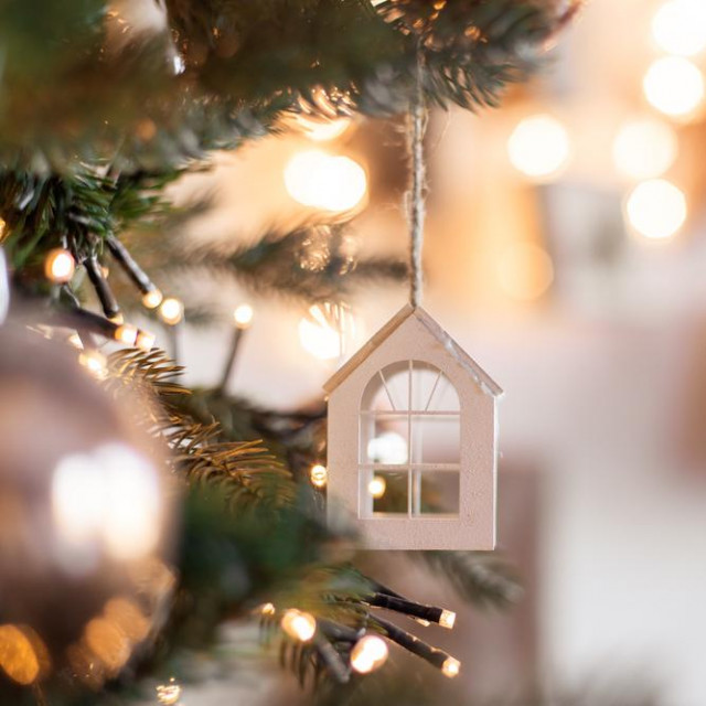 Christmas tree toy in the form of a house on a branch. Christmas mood background. Vacation atmosphere. Comfort hyuge concept cozy. Family budget Mortgage buying real estate