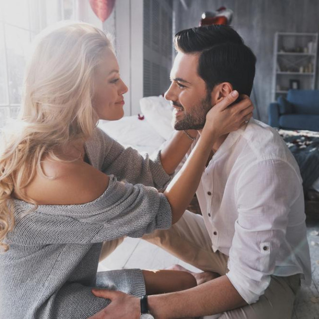 She is the center of his universe. Beautiful young couple looking at each other while sitting in the bedroom