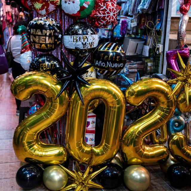 A woman uses her cell phone as she walks past balloons and 2023 signs while shopping at the San Jacinto market in the historic center of Caracas on December 30, 2022, on the eve of the end-of-the-year celebrations. (Photo by Yuri CORTEZ/AFP)