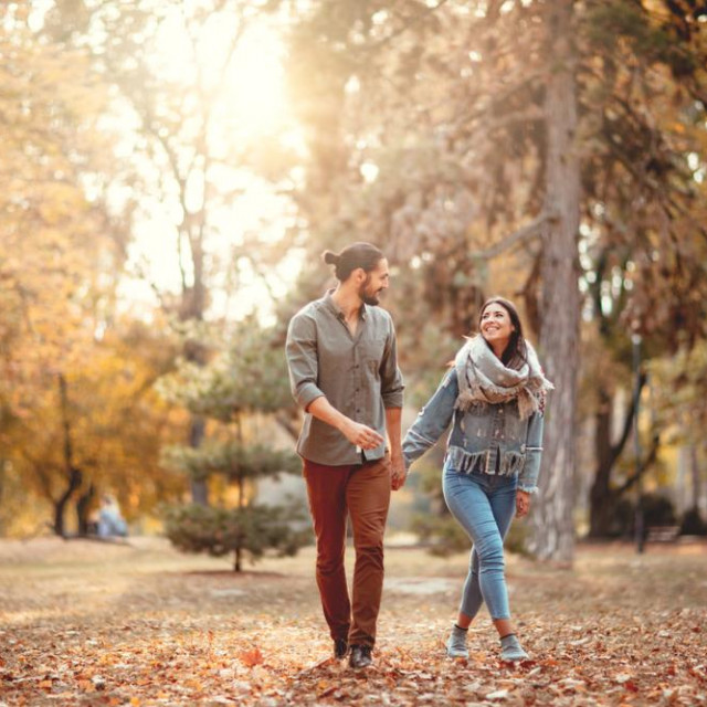 Beautiful smiling couple enjoying in sunny city park in autumn colors looking each other.
