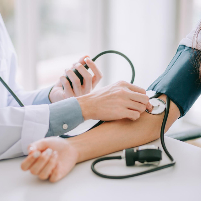 Doctor using sphygmomanometer with stethoscope checking blood pressure to a patient in the hospital.