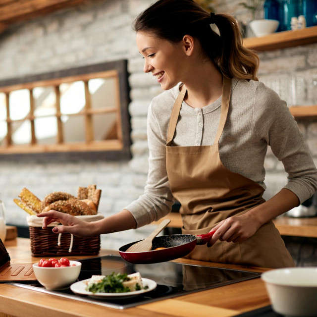 Happy woman preparing food while following recipe on digital tablet in the kitchen.