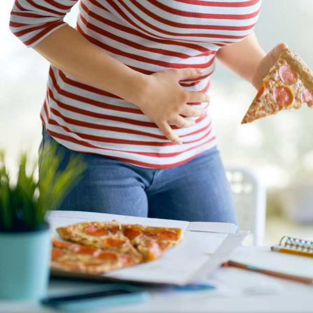Woman eating pizza on the desk at work and having stomach problems.