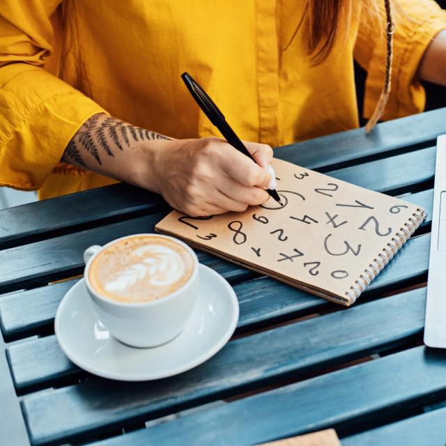 Woman freelancer writing numbers in notepad while working with laptop in street cafe. Time Management