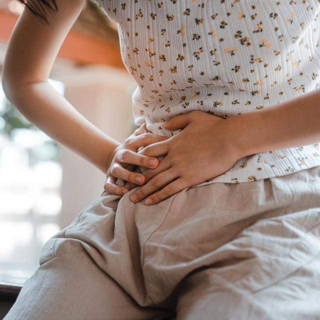 People pain at home concept. Young adult woman have stomach ill from period menstruation on day time. Hand touch on body.