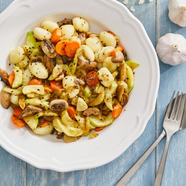 Tasty homemade vegan gnocchi with fresh vegetables. carrot, zucchini, mushrooms and olive oil, served on a modern ceramic plate, with seasoning and herbs on a blue rustic wooden kitchen or restaurant table, representing a healthy lifestyle, wellbeing and body care, top view with a copy space