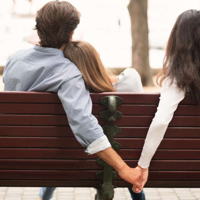 Love Triangle. Cheating Boyfriend Hugging Girlfriend Holding Hands With Her Girl Friend Sitting On Bench Together In Park Outdoor. Back-View