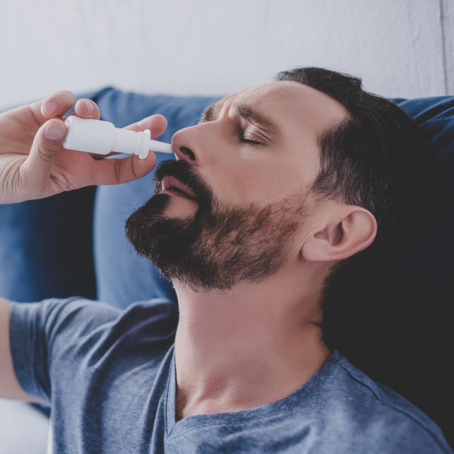 portrait of man sitting in the bed spraying drops in his nose