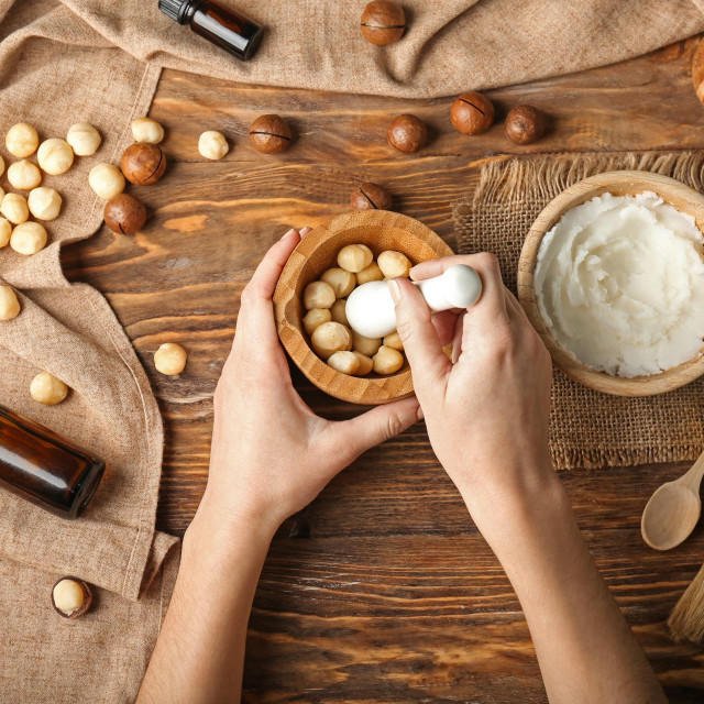 Woman pounding macadamia nuts in mortar on wooden table