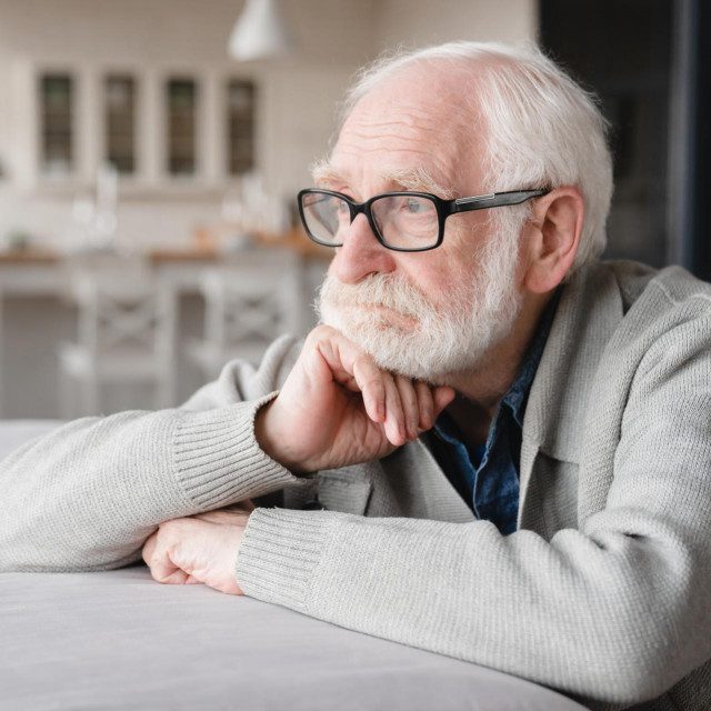 Sad tired ill sick lonely disappointed caucasian old elderly senior man grandfather sitting on the sofa couch, feeling nostalgy, pain, missing grandchildren, bankruptcy, fraud at home