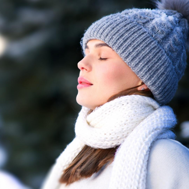 Side beauty portrait of beautiful attractive girl, young calm woman is breathing deep deeply fresh air at winter cold frosty snowy day with her eyes closed, meditating, doing breath exercise, enjoying