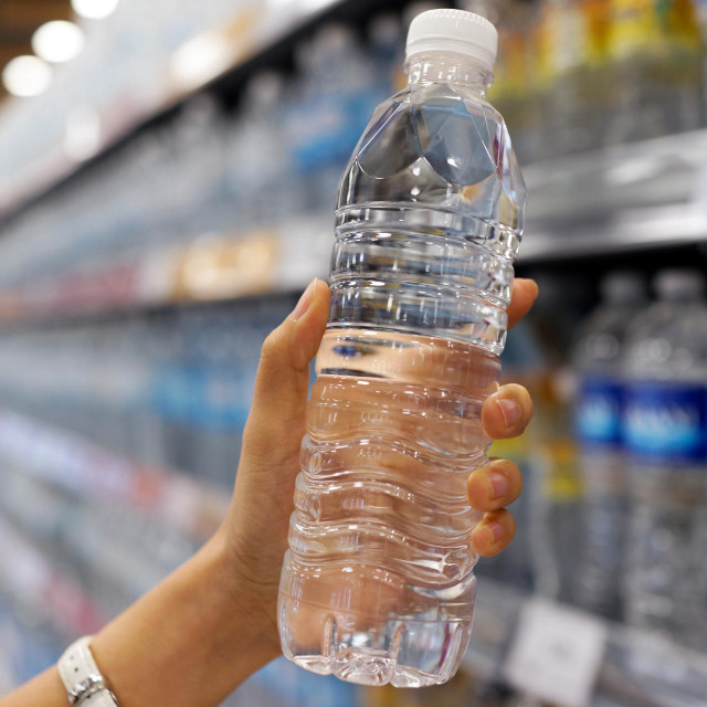 Close up female hand holding a bottle of water or mineral water in grocery store.