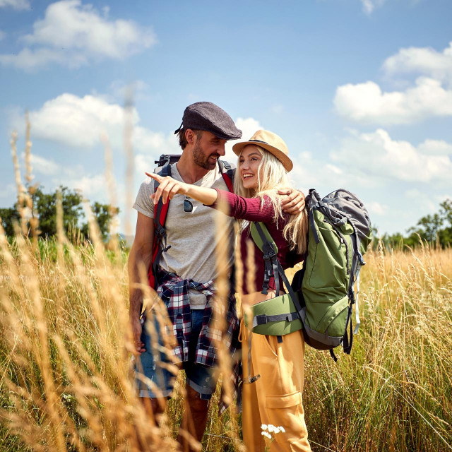 Young couple hiking with backpack in field. Sport, freedom, holiday concept.