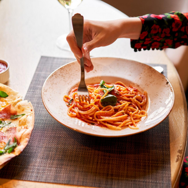 Italian Trattoria. Woman eats Italian pasta with tomato, meat. Spaghetti Bolognese wind it around a fork with a spoon. Parmesan cheese