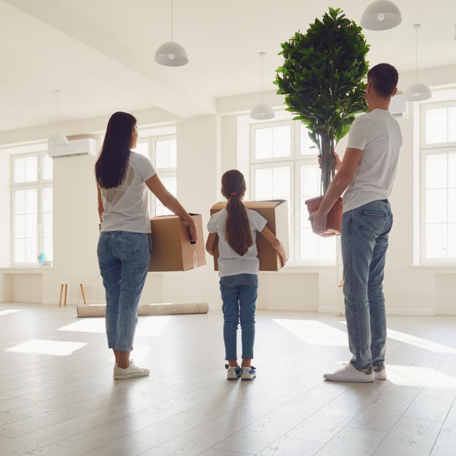 Happy family with children moving with boxes in a new apartment house. Back view.