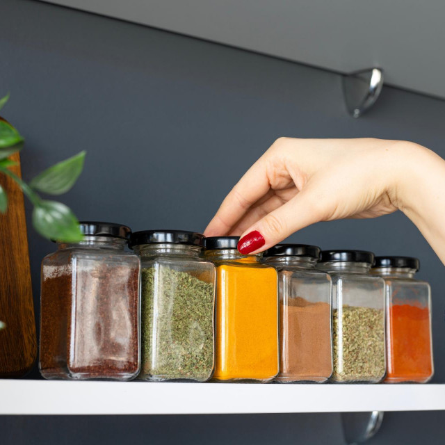 Cropped hand holding jar of spices on kitchen.