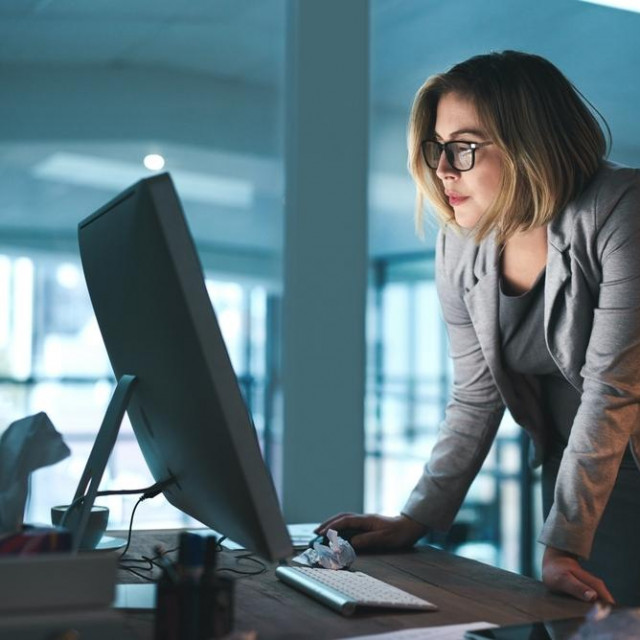 Woman, employee and reading on computer in office on browsing internet, online and research for ideas. Female person, workplace and desk with deadline or overtime, project and standing as hr