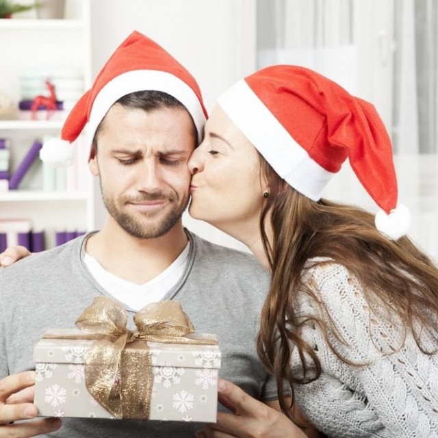 boyfriend looks skeptical to his christmas gift while his girlfriend give him a kiss