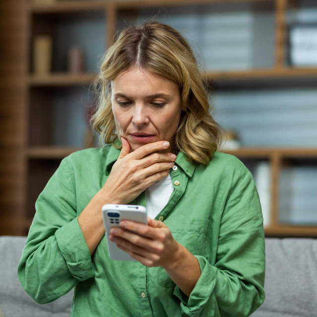 Close-up photo. Worried senior woman mother sitting on sofa at home and holding phone. Worries about children, writes and sends messages, calls, searches, waits at home.
