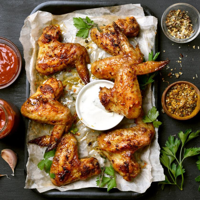 Baked chicken wings on baking tray over dark background, top view