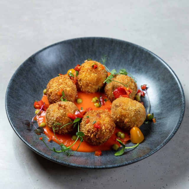 Arancini rice balls with tomato sauce and pea purée plated on a grey plate