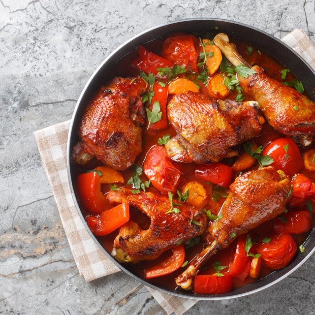 Homemade rooster stew with bell peppers, onions and carrots in a spicy tomato sauce close-up in a pan on the table. Horizontal top view from above