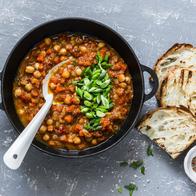 Vegetarian mushrooms chickpea stew in a iron pan and rustic grilled bread on a gray background, top view. Healthy vegetarian food concept. Vegetarian chili