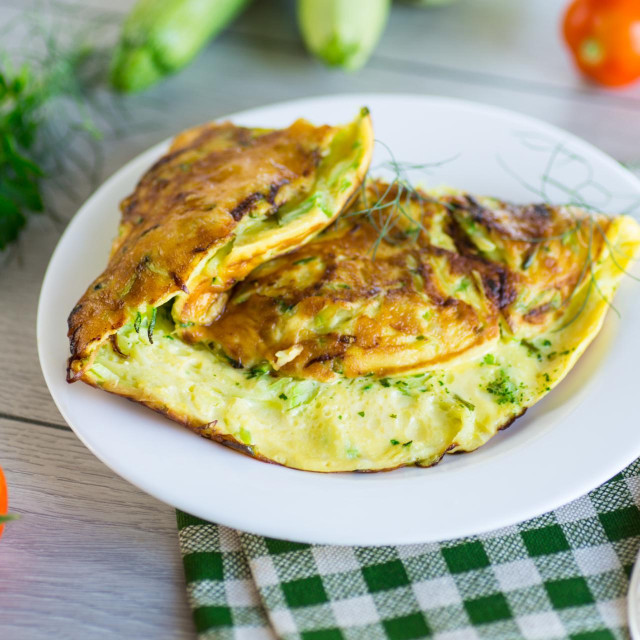 Fried omelet with zucchini,in a plate on a wooden table.