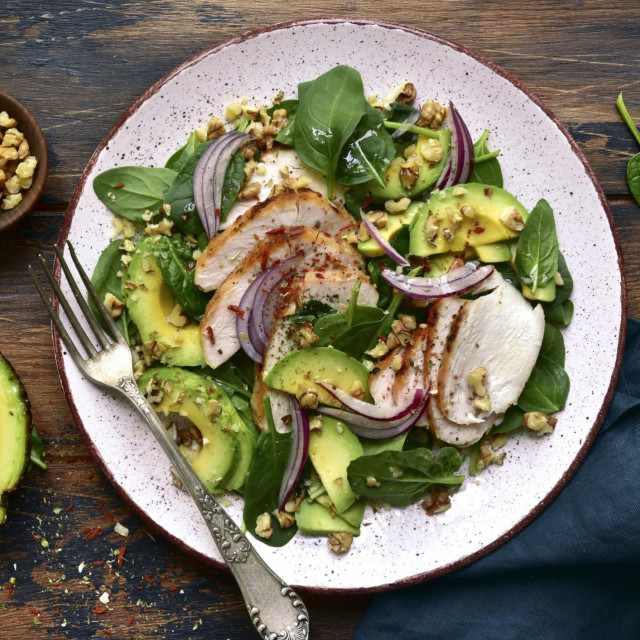 Spinach salad with grilled chicken fillet, avocado and walnuts on a plate over dark wooden background.Top view with copy space.