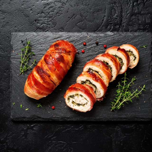 Bacon wrapped chicken rolls stuffed with feta cheese and spinach on black stone background. Beautiful festive lunch or dinner. top view