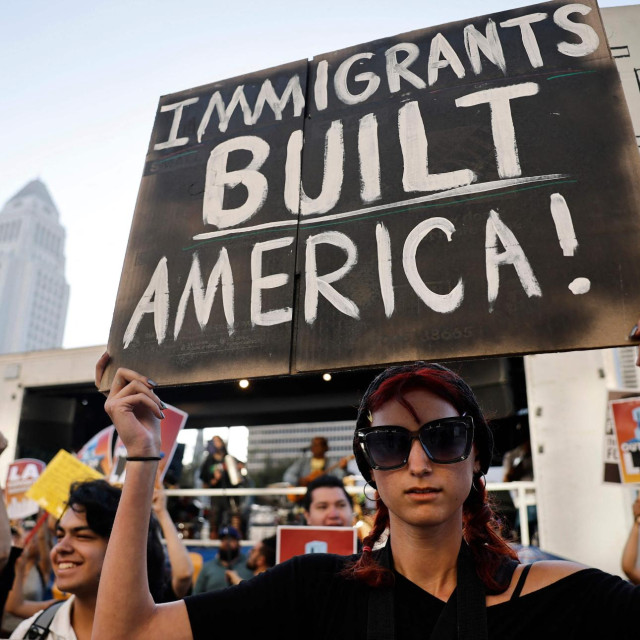 Prosvjednik nosi transparent s natpisom „Imigranti su izgradili Ameriku!” tijekom prosvjeda protiv ICE-a ispred savezne zgrade u Los Angelesu. Demonstracije dolaze istoga dana kada je savezni prizivni sud odobrio nastavak raspoređivanja oko 4.000 pripadnika Nacionalne garde, prema odluci predsjednika Trumpa