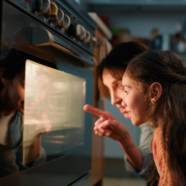 Mom, girl and check oven in kitchen for baking, cake or muffins with pointing, learning and teaching. Stove, mother and daughter with support, bonding and love with smile for food in family house